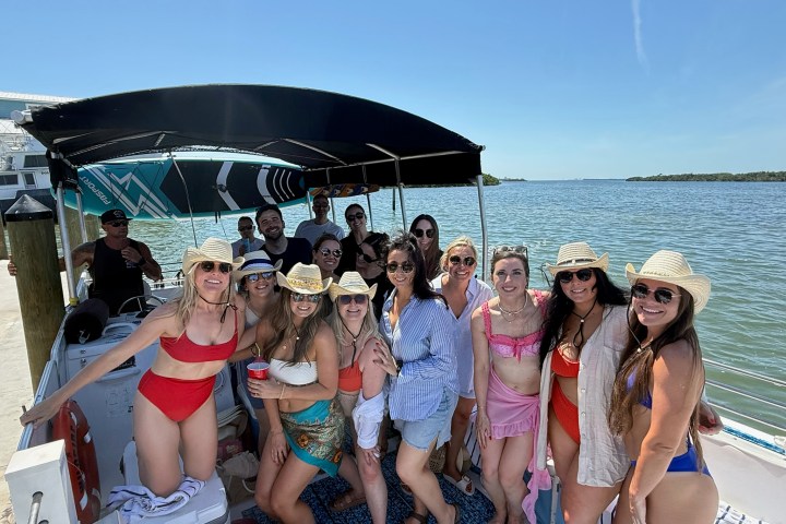Group of people in swimwear and hats on a boat near water.