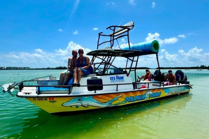 People on dolphin tour boat in clear green water under blue sky.