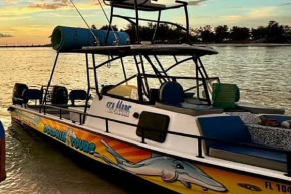 Colorful tour boat docked on sandy beach at sunset with scenic, cloudy sky.
