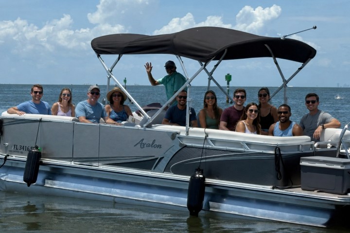Group of people sitting on a pontoon boat in open water on a sunny day.