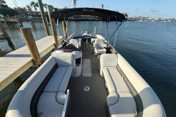Open pontoon boat docked on calm water under clear sky.