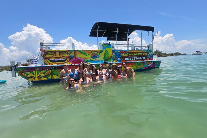 Group in water near a colorful boat under clear blue sky.