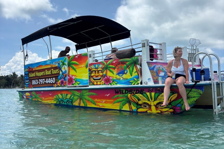 Colorful boat with canopy on water, woman sitting at the stern, cloudy sky.